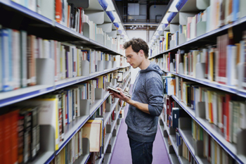 Sportstudent steht in Bibliothek und sucht nach einem Buch