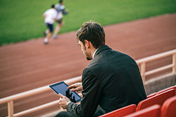 Mann im Anzug sitzt mit einem Tablet im Stadion.