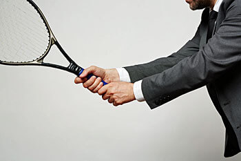 Mann im Anzug hält Tennisschläger in der Hand.